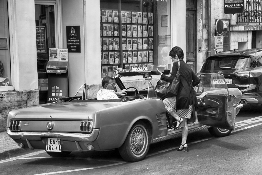 Middle-aged woman getting up into old sport car from early 70's