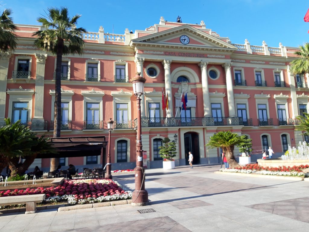 A colonial-style three-story building with a decorative square in front.