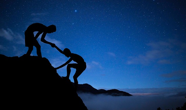 A mountaineer helps another climb to the top.